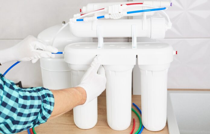 Instalación sistema de ósmosis de purificación. Plomero o mano de hombre reemplaza los cartuchos de filtro de agua en la cocina de casa. De cerca.